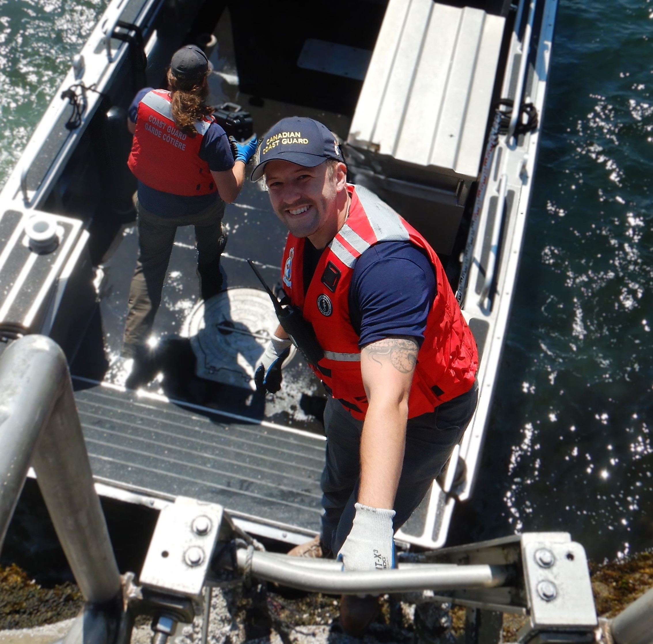 Two Canadian Coast Guard workers on a boat, one smiling up at the camera.