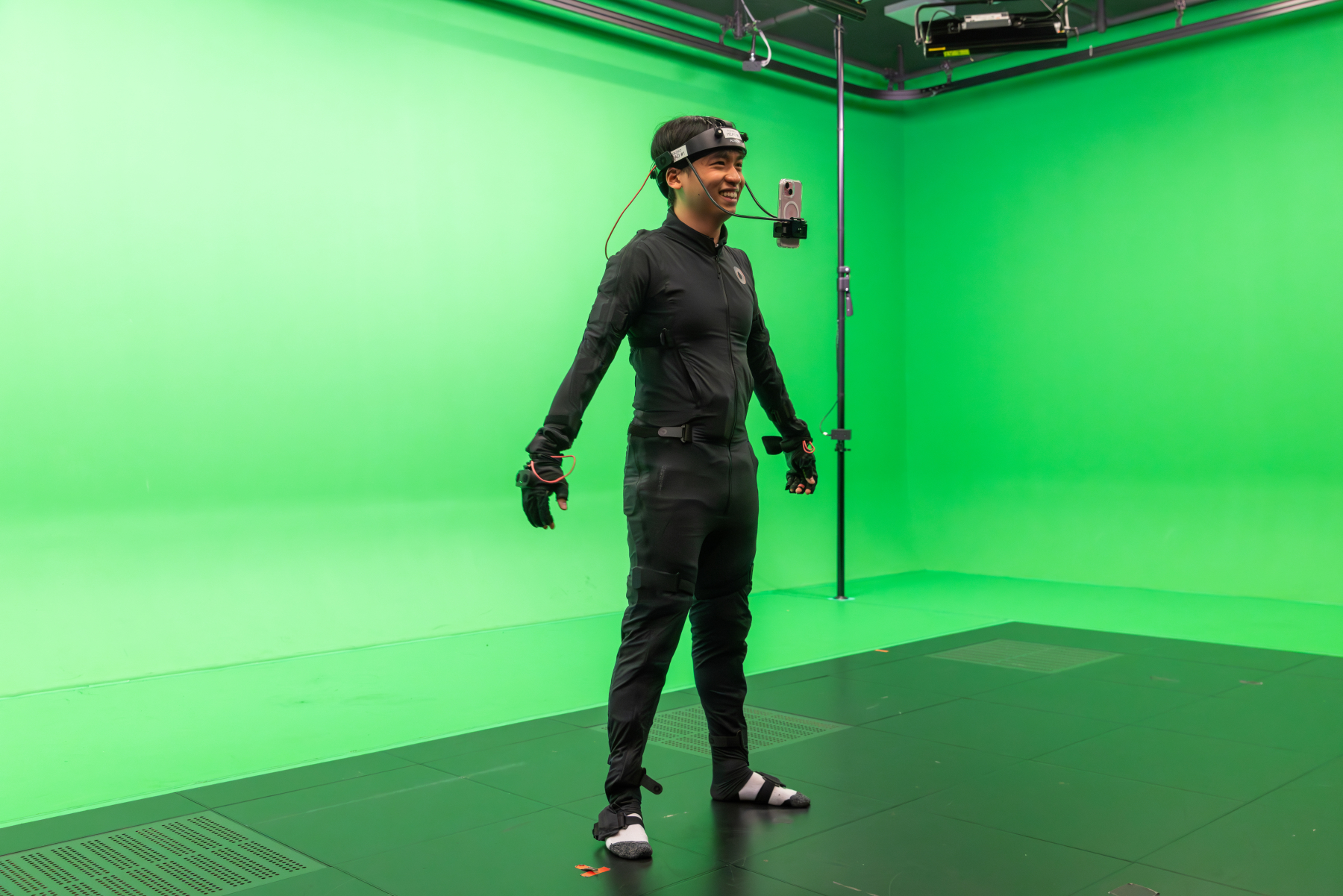 A person in a motion-capture suit and head-mounted equipment stands in a green-screen studio.