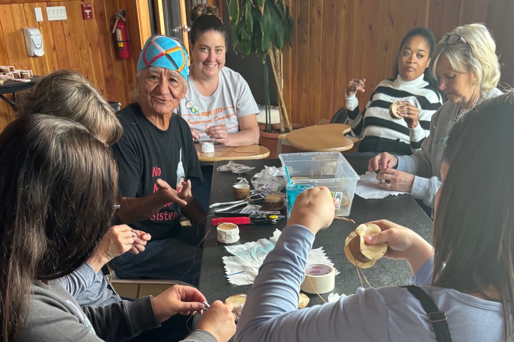 A group of adults sit around a table indoors, preparing or sharing food during a communal activity.